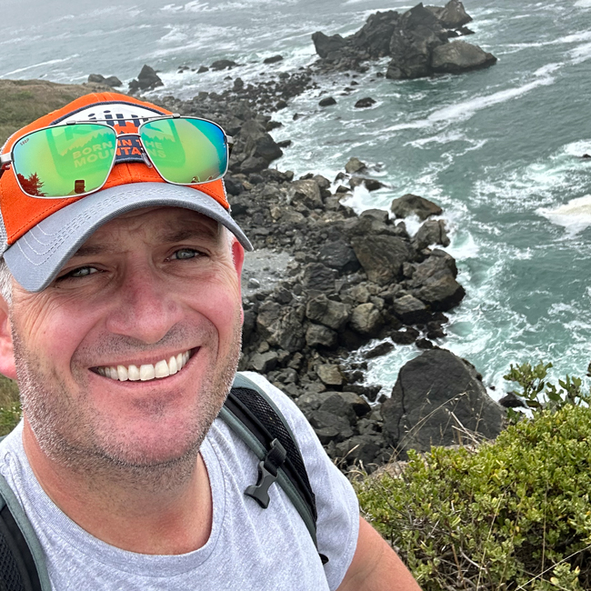 John Chastain on a hike, in front of rocky water.