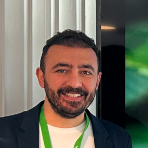 Headshot of Dr. Burak Akyüz, man with dark hair, beard and mustache, smiling, wearing black blazer and white t-shirt.