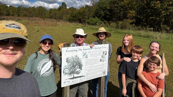 Volunteers gather around American chestnut restoration sign.