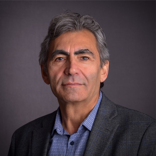 Man with grey blazer, blue shirt, and dark grey hair. Headshot of Fikrit Isik.